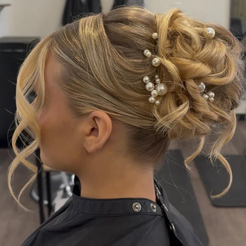 A side view of a pearl-pinned blonde updo with soft face-framing curls